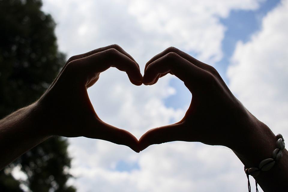 hands making a heart with a cloudy blue background
